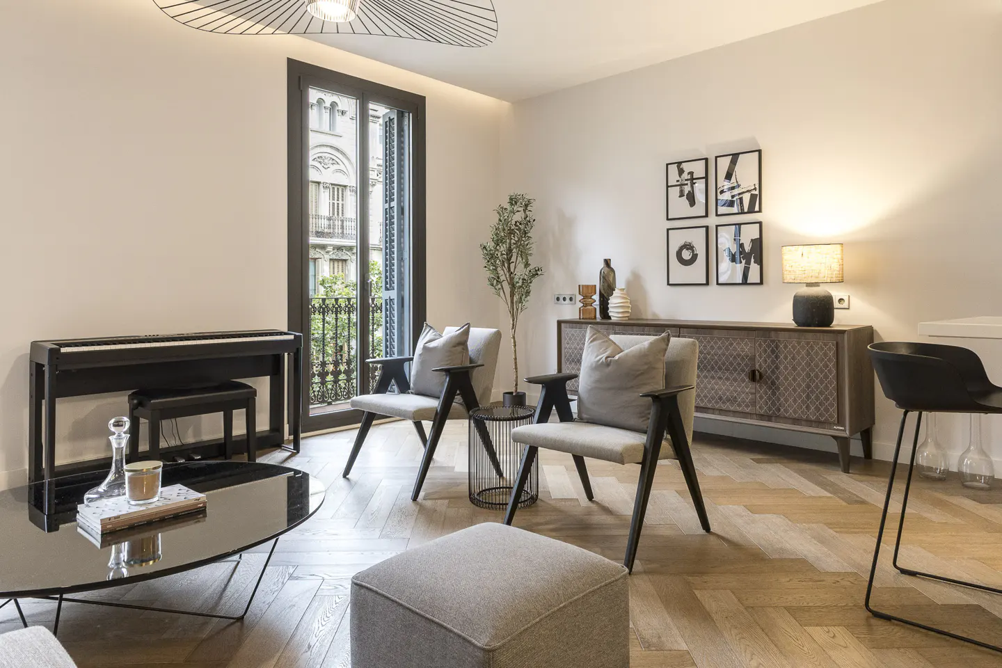 A bright living room with a piano, two chairs, a black coffee table, and a wooden floor.