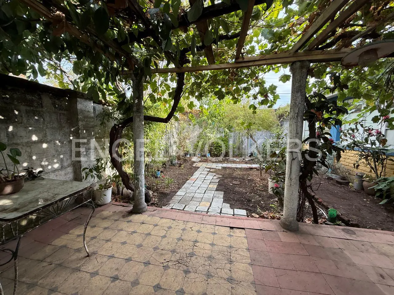 Outdoor patio with a stone path leading to a garden, covered by a vine-covered pergola.