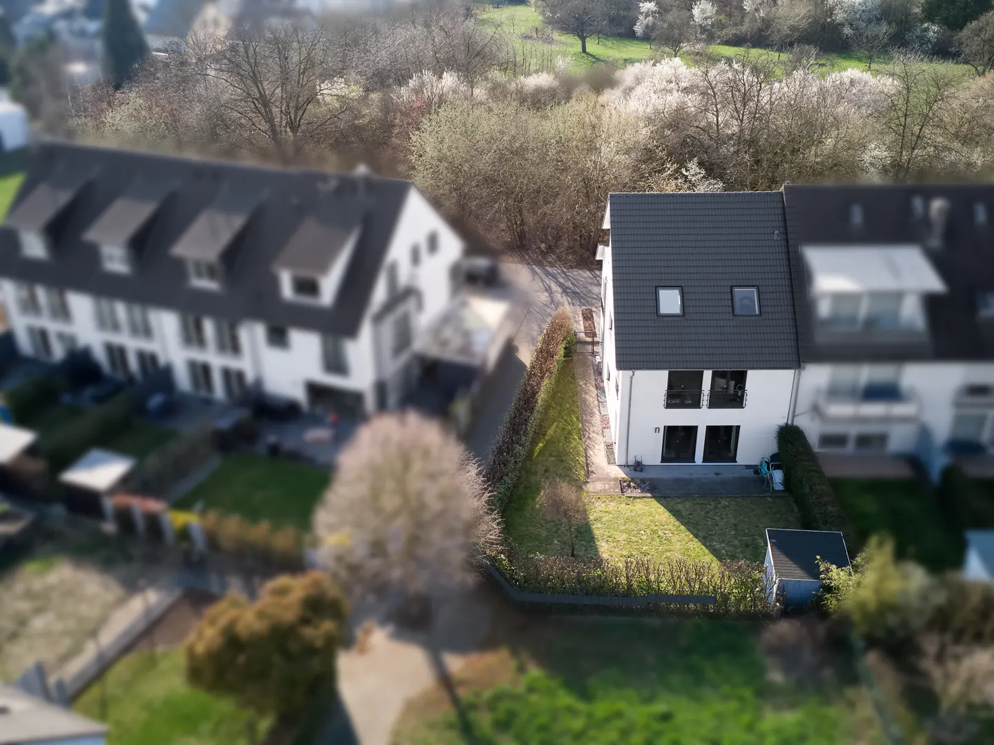 Aerial view of a white two-story townhouse with a gray roof and a green lawn, surrounded by trees and other houses.