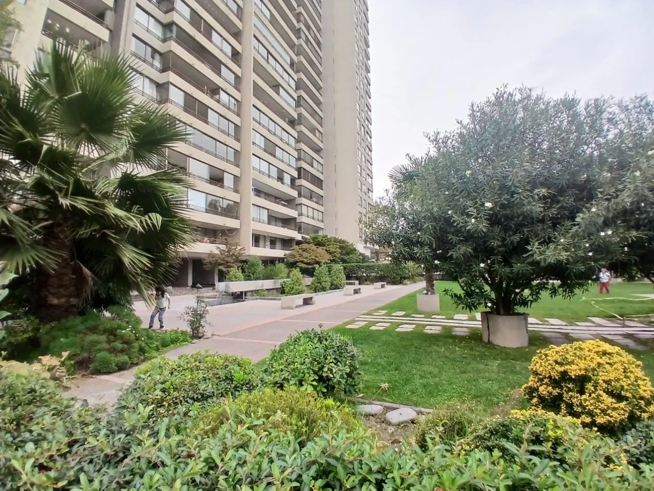 View of a tall apartment building with a green lawn, trees, and a walkway in front.