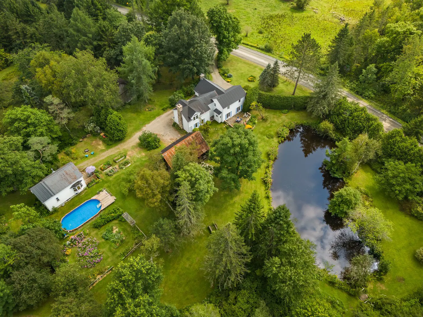 Aerial view of a white house with a pond, pool, and garden surrounded by lush green trees.