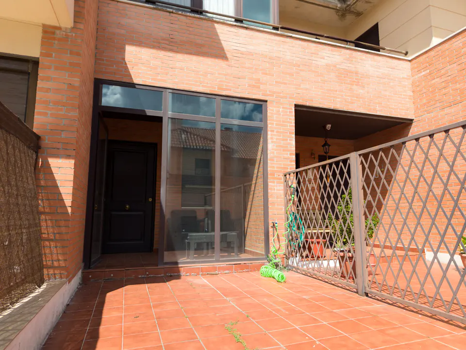 Brick patio with a black door and metal fence. A green hose is coiled on the patio.