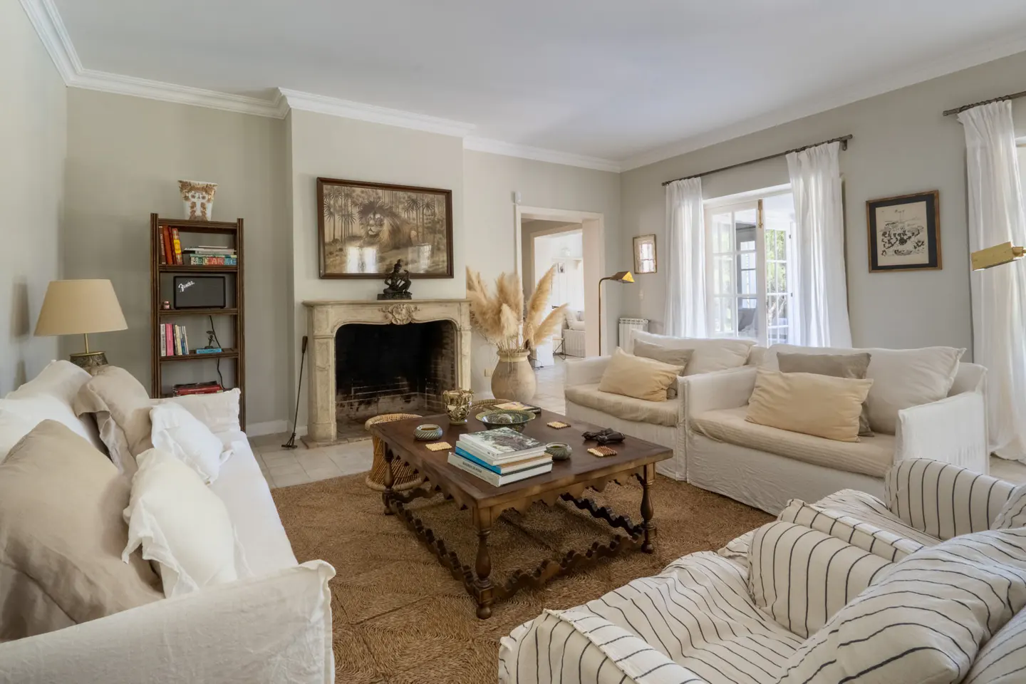 Living room with white sofas, a wooden coffee table, and a stone fireplace. A bookshelf and artwork add character to the neutral-toned space.