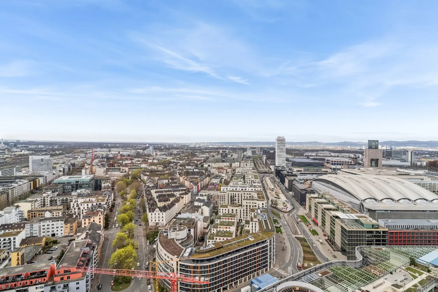 Cityscape view with buildings, roads, and a blue sky. A large convention center with a curved roof is visible.