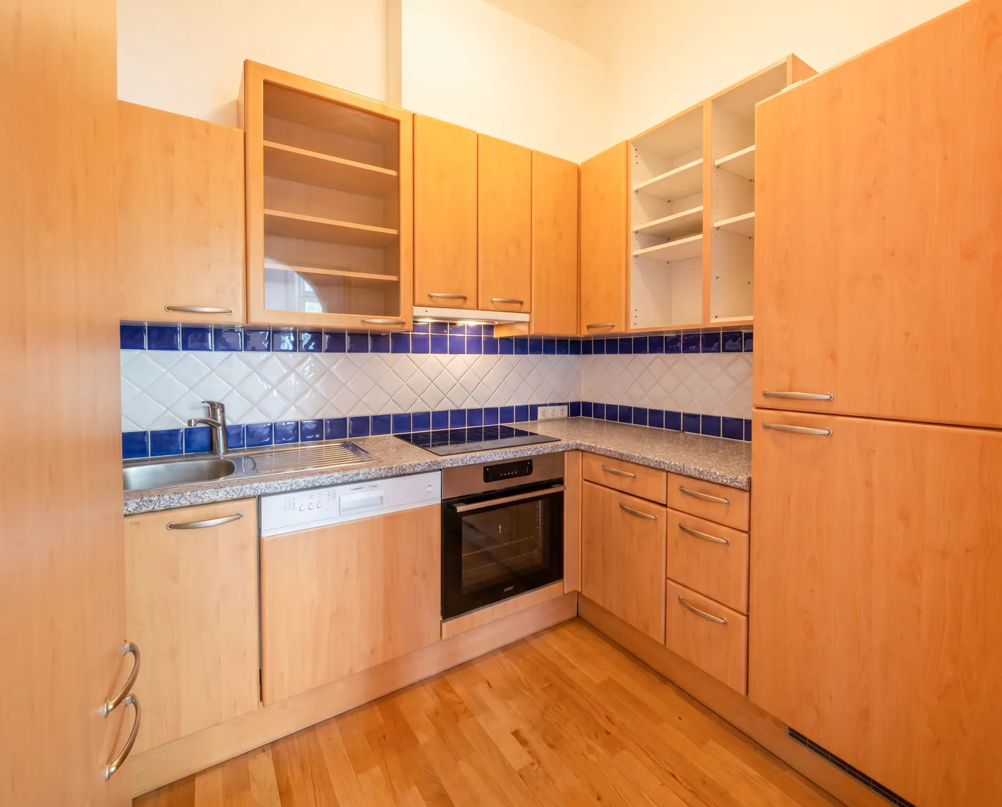 A bright kitchen with light wood cabinets, stainless steel appliances, and blue and white tiled backsplash.