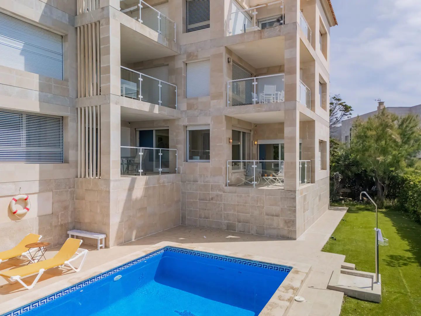 Multi-story stone building with balconies overlooking a blue swimming pool, lawn, and outdoor shower.