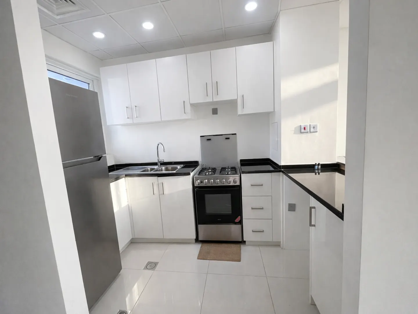 A bright kitchen with white cabinets, black countertops, and stainless steel appliances. A refrigerator is on the left, and a stove is on the right.