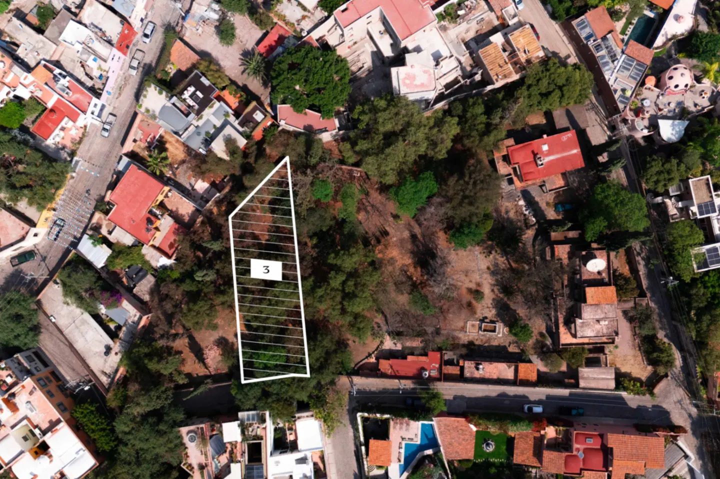 Aerial view of a vacant lot marked with white lines and the number 3, surrounded by trees and buildings.