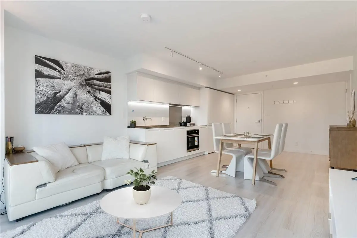 Bright, modern apartment interior with white walls, furniture, and a geometric rug. A black and white tree art piece hangs above the white sofa.