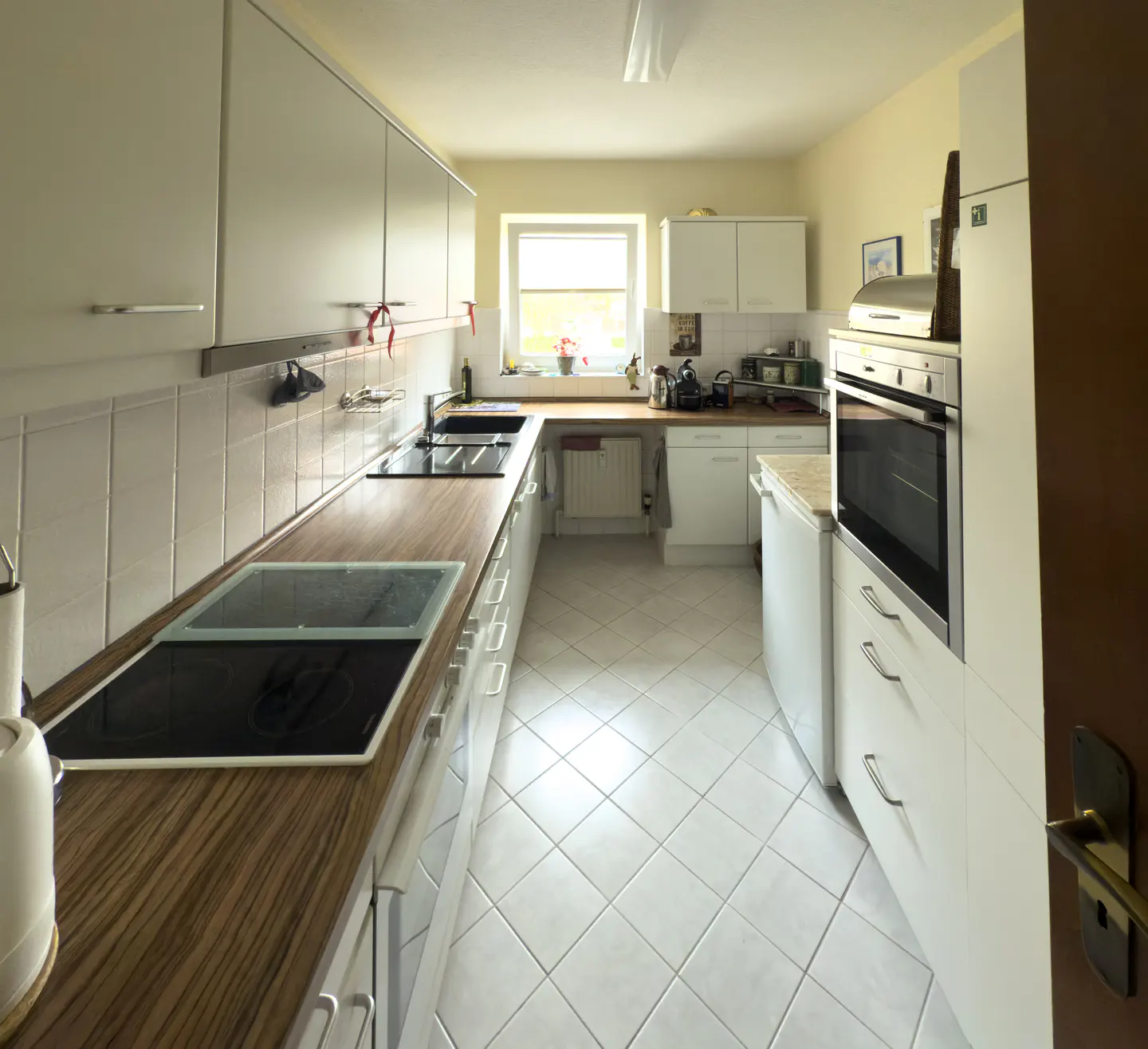 Bright kitchen with white cabinets, wood countertops, and white tiled floors. A window is visible in the background.