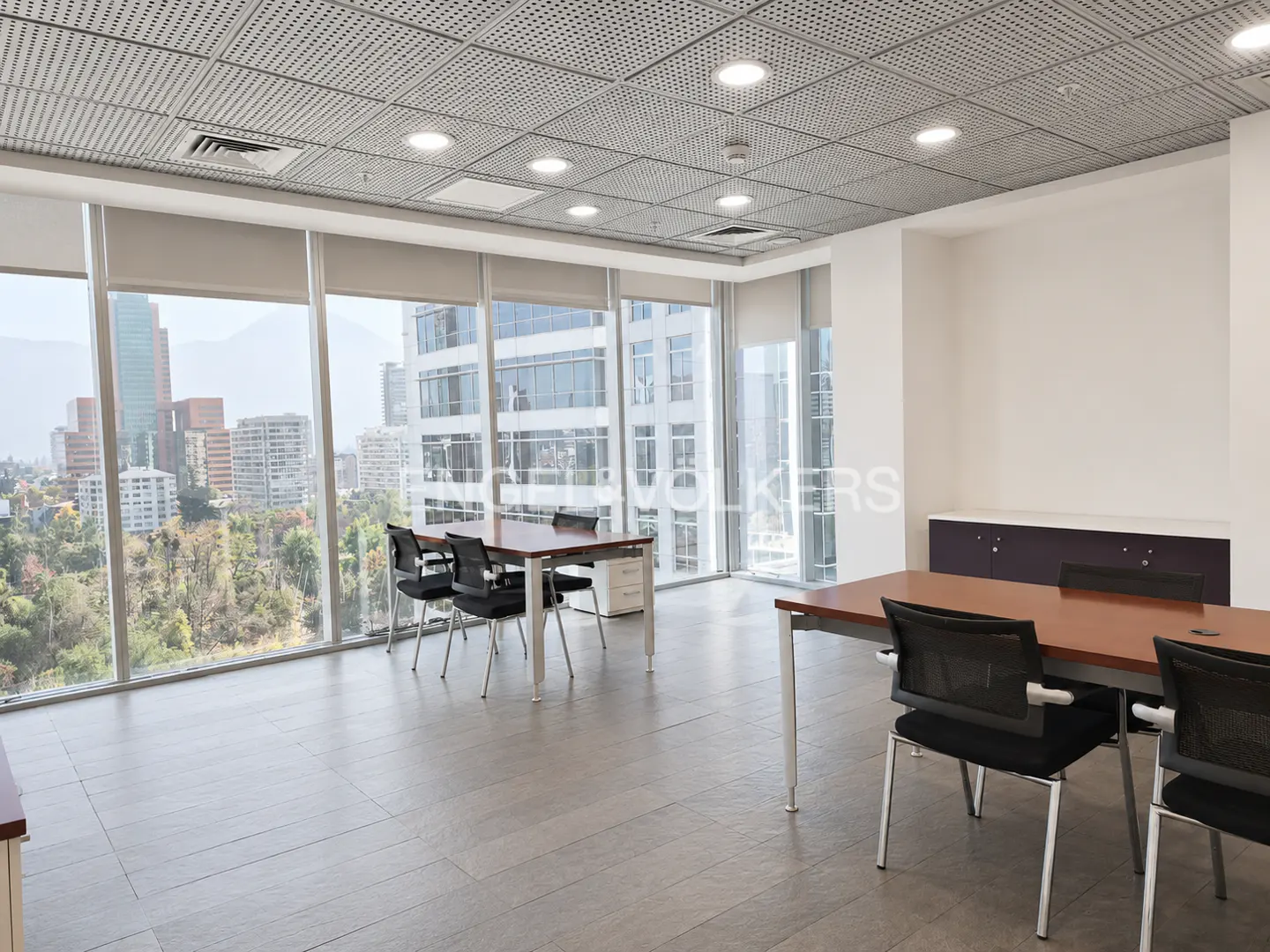 Bright office space with large windows showing city views. Tables and chairs are arranged in the room.