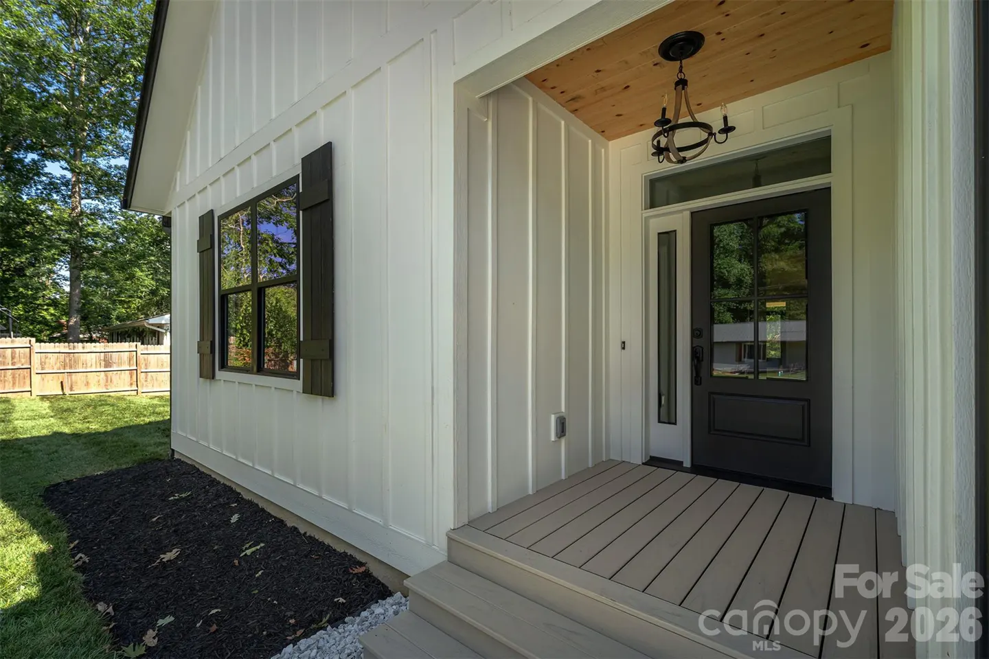 Exterior of a white house with a black front door, window with shutters, and a wooden porch.