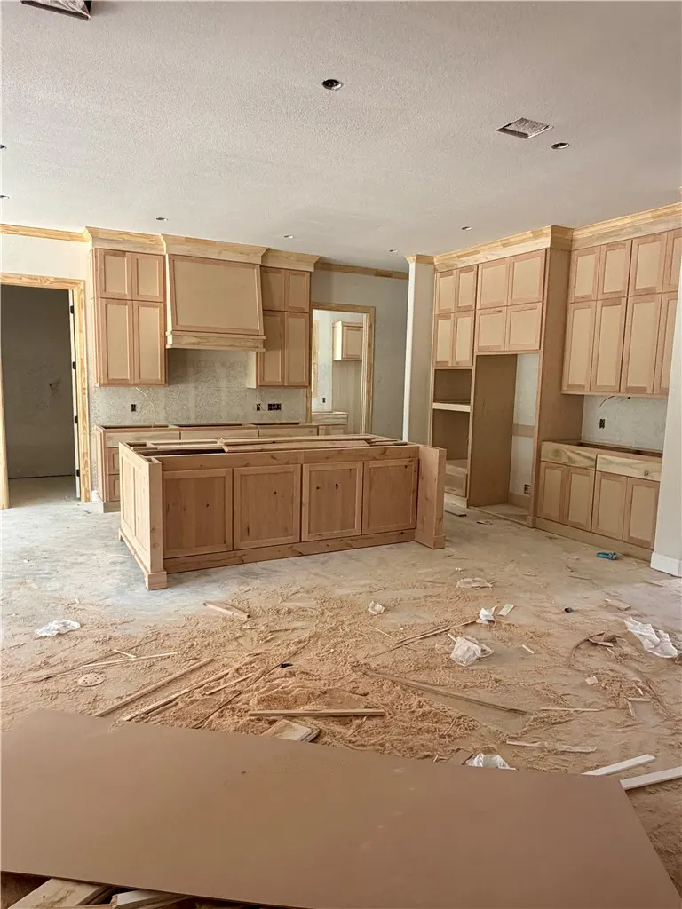 Kitchen under construction with unfinished light wood cabinets, a large central island, and sawdust covering the floor.