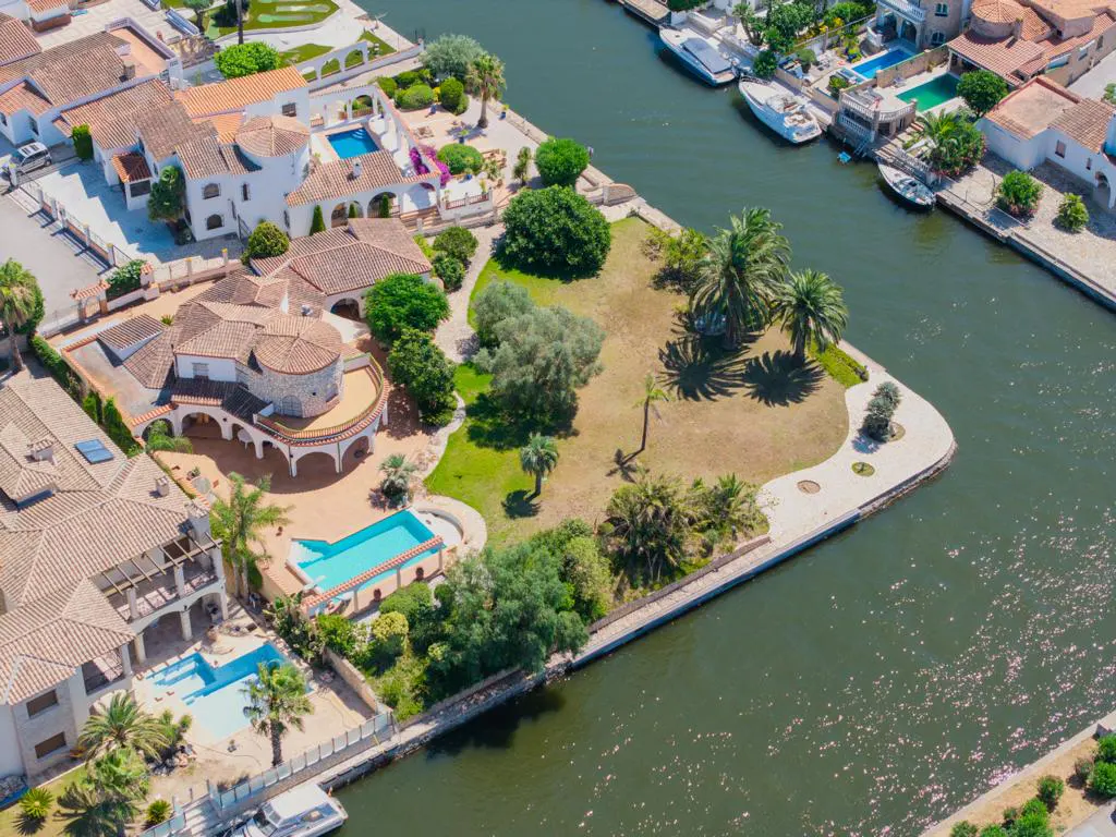 Aerial view of a waterfront villa with a large garden, swimming pool, and private dock on a canal with moored boats.