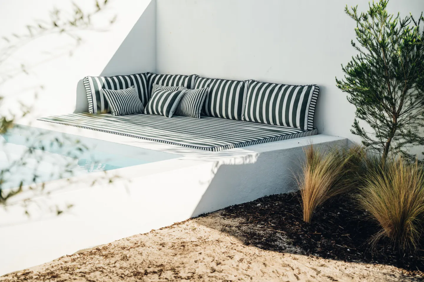 Outdoor lounge area with black and white striped cushions and pillows, next to a small pool and greenery.