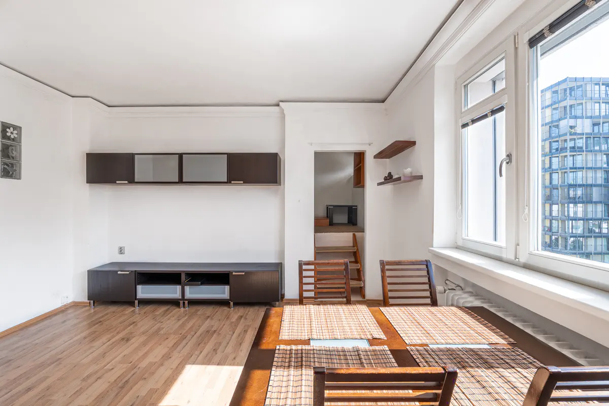 Dining area with wooden table, chairs, dark cabinets, and a view of a modern building through a large window.