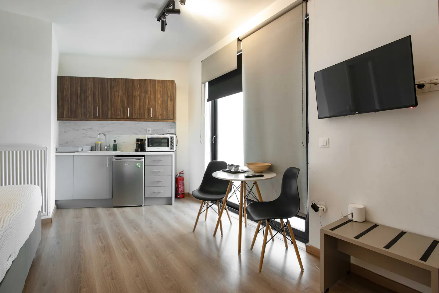 Studio apartment with kitchenette, table and chairs, and TV. Wood-look floors and cabinets.