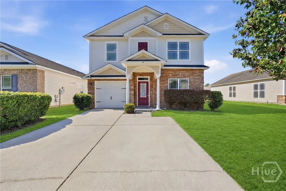 Two-story house with white siding, stone accents, a red front door, and a concrete driveway on a sunny day.