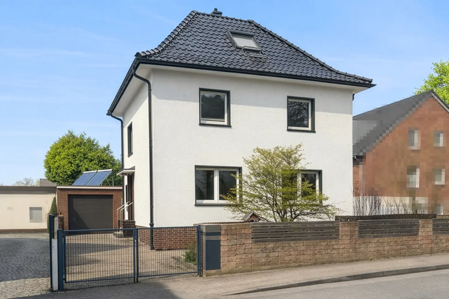 Two-story white house with a black roof and trim, a brick fence, and a metal gate.