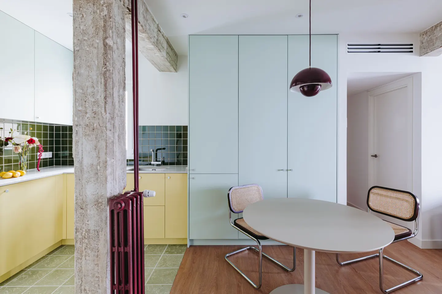 A modern kitchen and dining area with yellow cabinets, a concrete pillar, and a white oval table with two chairs.