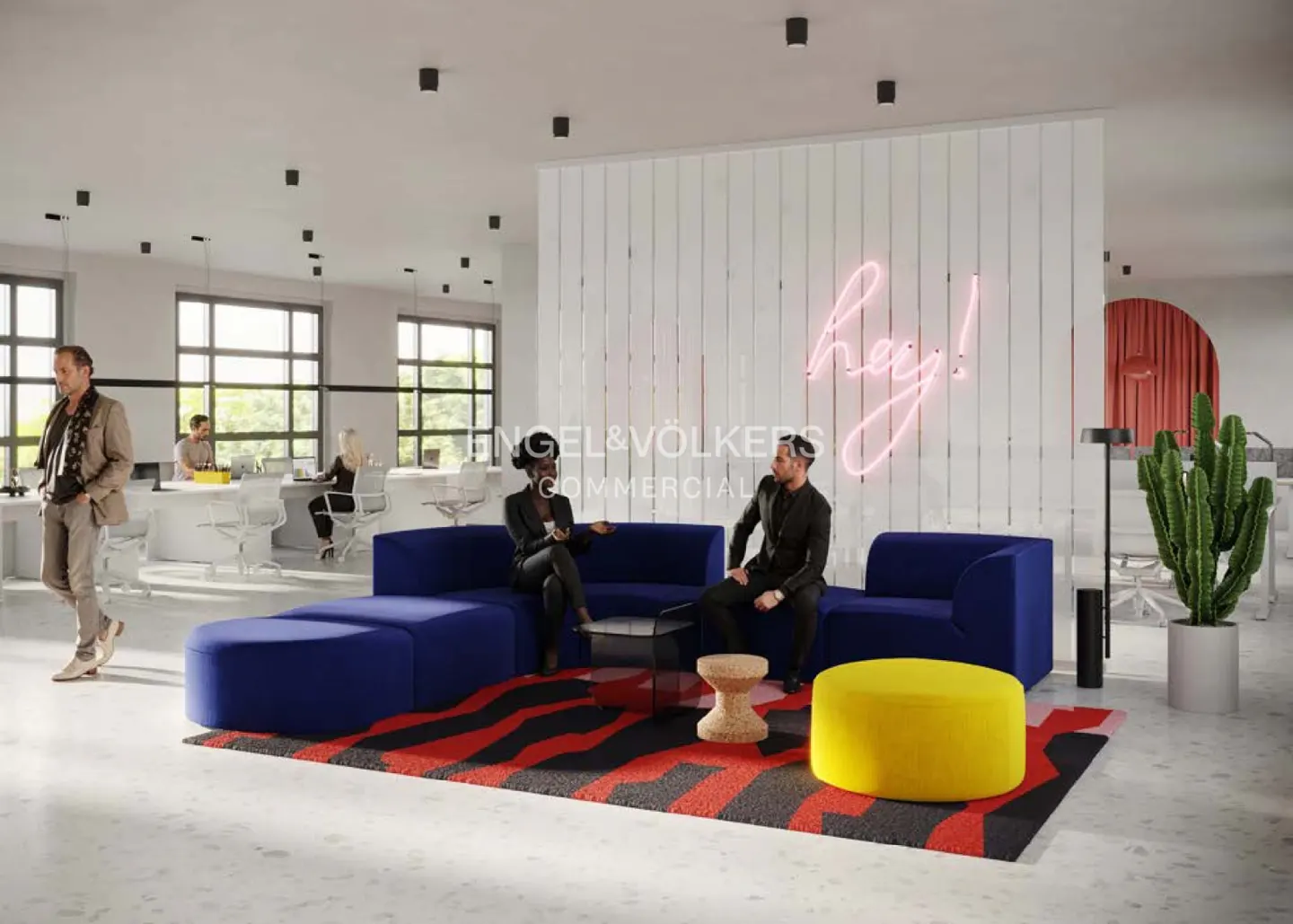 Office lounge area with blue sofas, a yellow ottoman, and a red and black rug. People are sitting and working in the background. A neon "hey!" sign is on the wall.