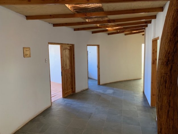 Interior view of a home with white walls, gray tile floors, and exposed wood beams on the ceiling. Several open wooden doorways are visible.