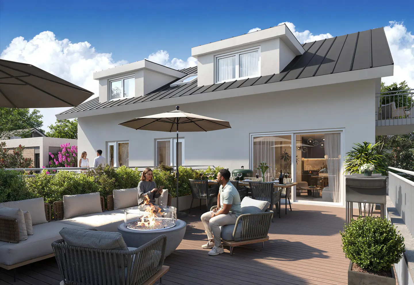 Outdoor patio with seating around a fire pit, dining table, and grill. A white building with a dark roof is in the background.