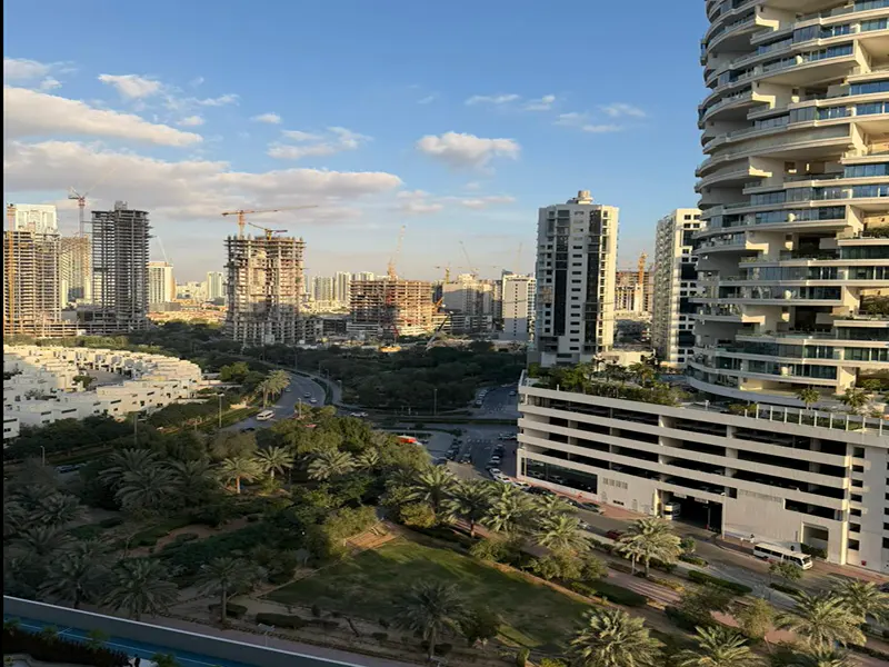 Cityscape view with modern buildings, palm trees, and construction cranes under a blue sky with scattered clouds.