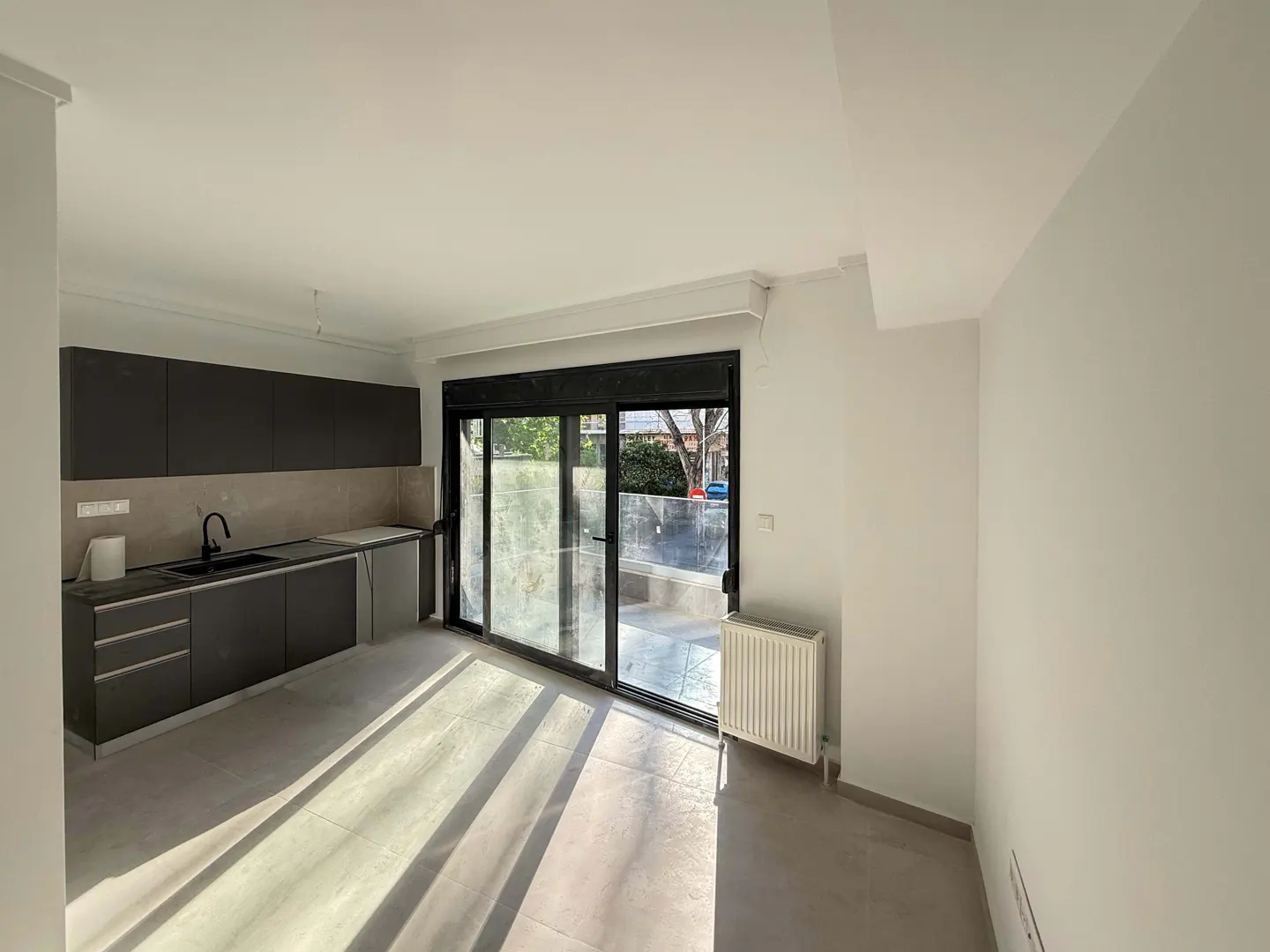 Bright, empty kitchen with dark cabinets, black sink, and sliding glass doors to a patio.