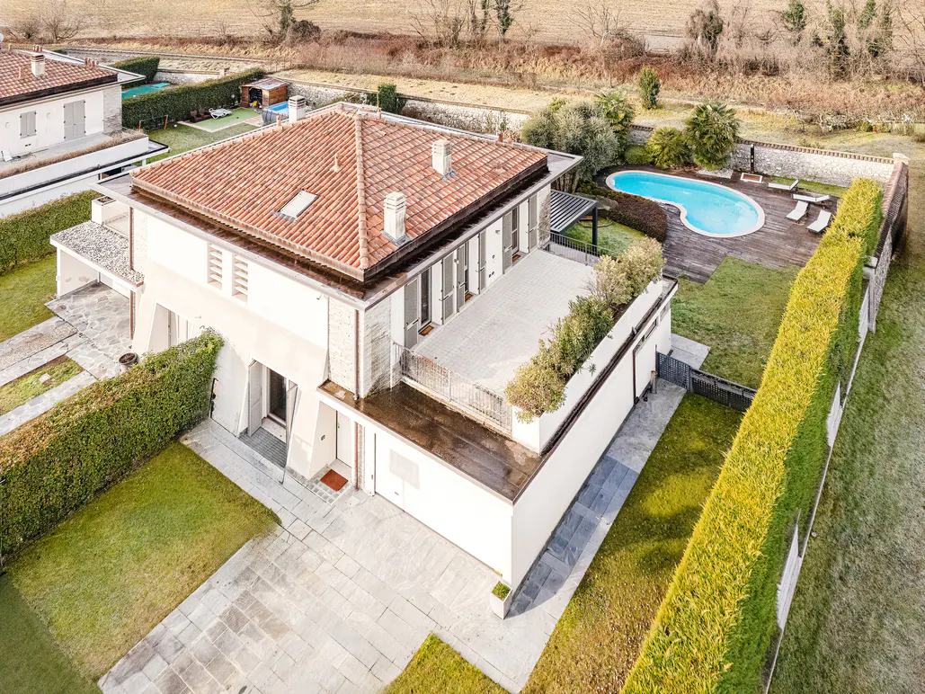 Aerial view of a modern, two-story white house with a red tile roof, a pool, and a green lawn.