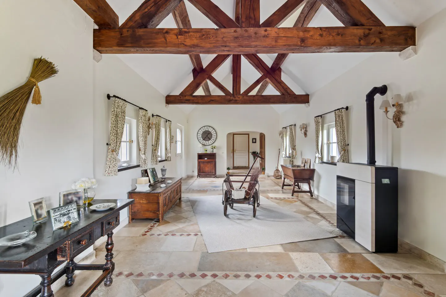 Spacious room with vaulted ceiling, exposed wooden beams, stone tile floor, antique furniture, and a modern pellet stove.