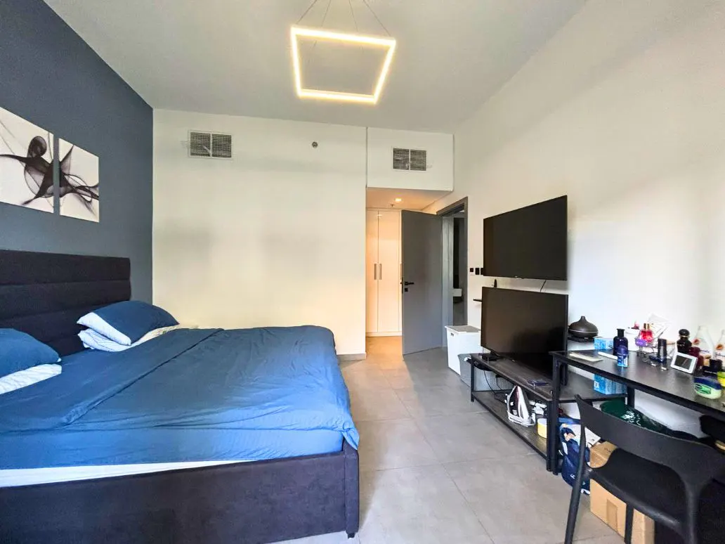 Bedroom with a blue bed, a desk with two TVs, and a square light fixture. The walls are white and blue.