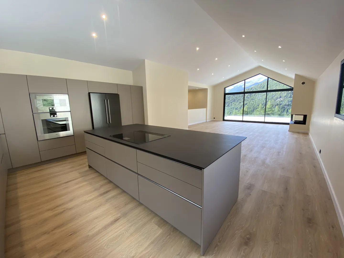 Modern kitchen with gray cabinets, black island countertop, and wood floors. Large window with mountain view.