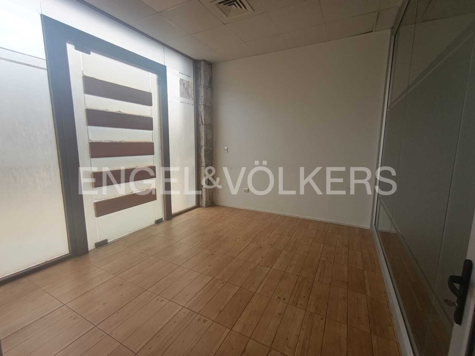 Empty office space with light wood-look tile flooring, white walls, and a modern glass door with horizontal brown panels.