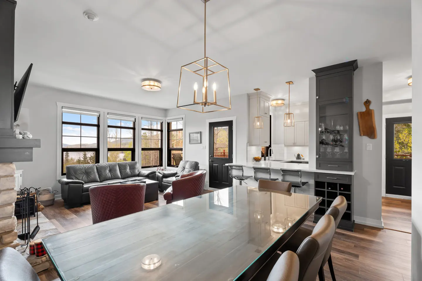Open-concept living area with a glass dining table, leather chairs, a black sofa, and a modern kitchen with a wine rack.