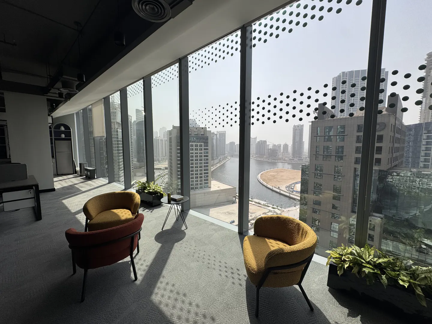 Bright office space with city view. Two armchairs, one yellow and one red, sit on a gray carpet near a large window.