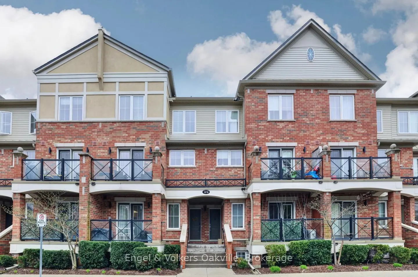 Exterior view of a brick townhouse with black railings, a small balcony, and a blue sky with white clouds.