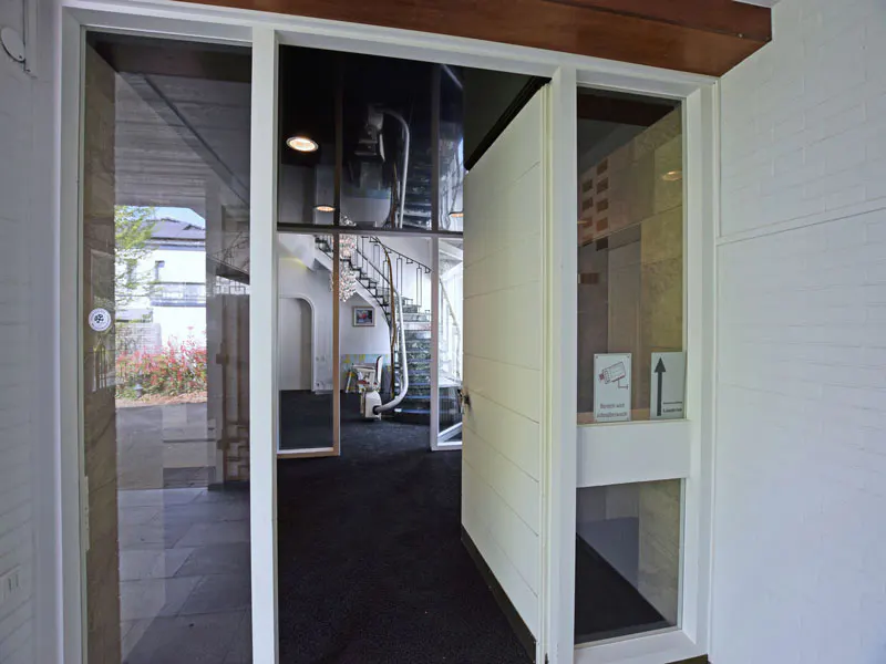 Open glass door reveals a modern interior with a spiral staircase and black carpet. White brick walls and a wooden beam add architectural detail.