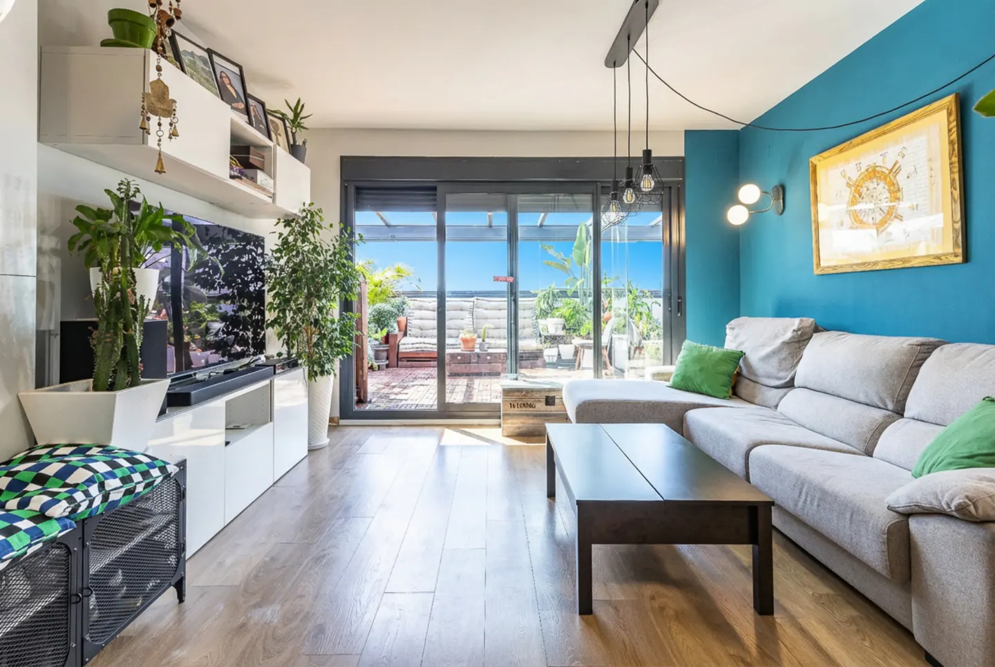 Bright living room with a gray sectional sofa, dark wood coffee table, and blue accent wall. Sliding glass doors lead to a sunny patio.