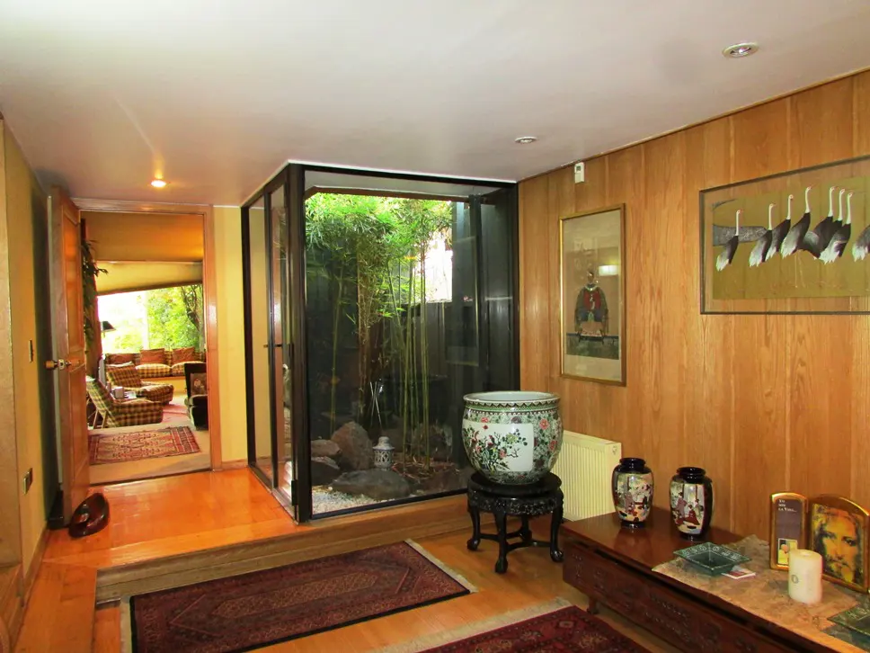 Interior view of a home with wood paneled walls, a glass enclosed garden, and a view into a living room.
