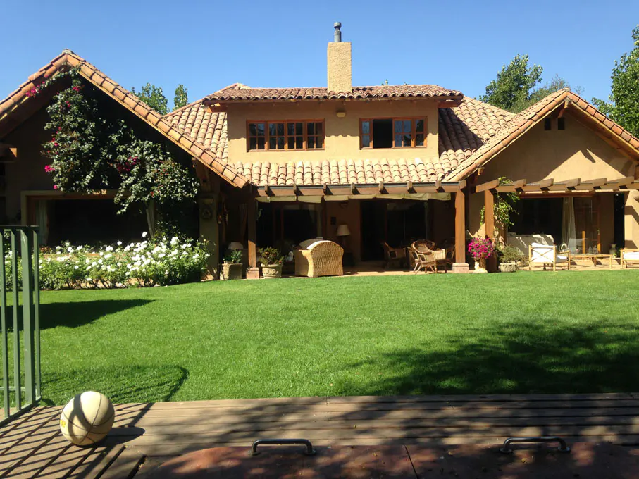 Exterior view of a tan stucco house with a red tile roof, green lawn, and patio furniture.