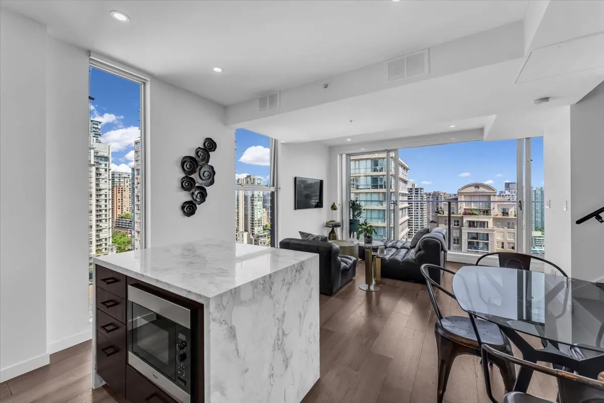 Bright condo interior with city views. Marble island, dark wood floors, and black furniture. Large windows show buildings and blue sky.