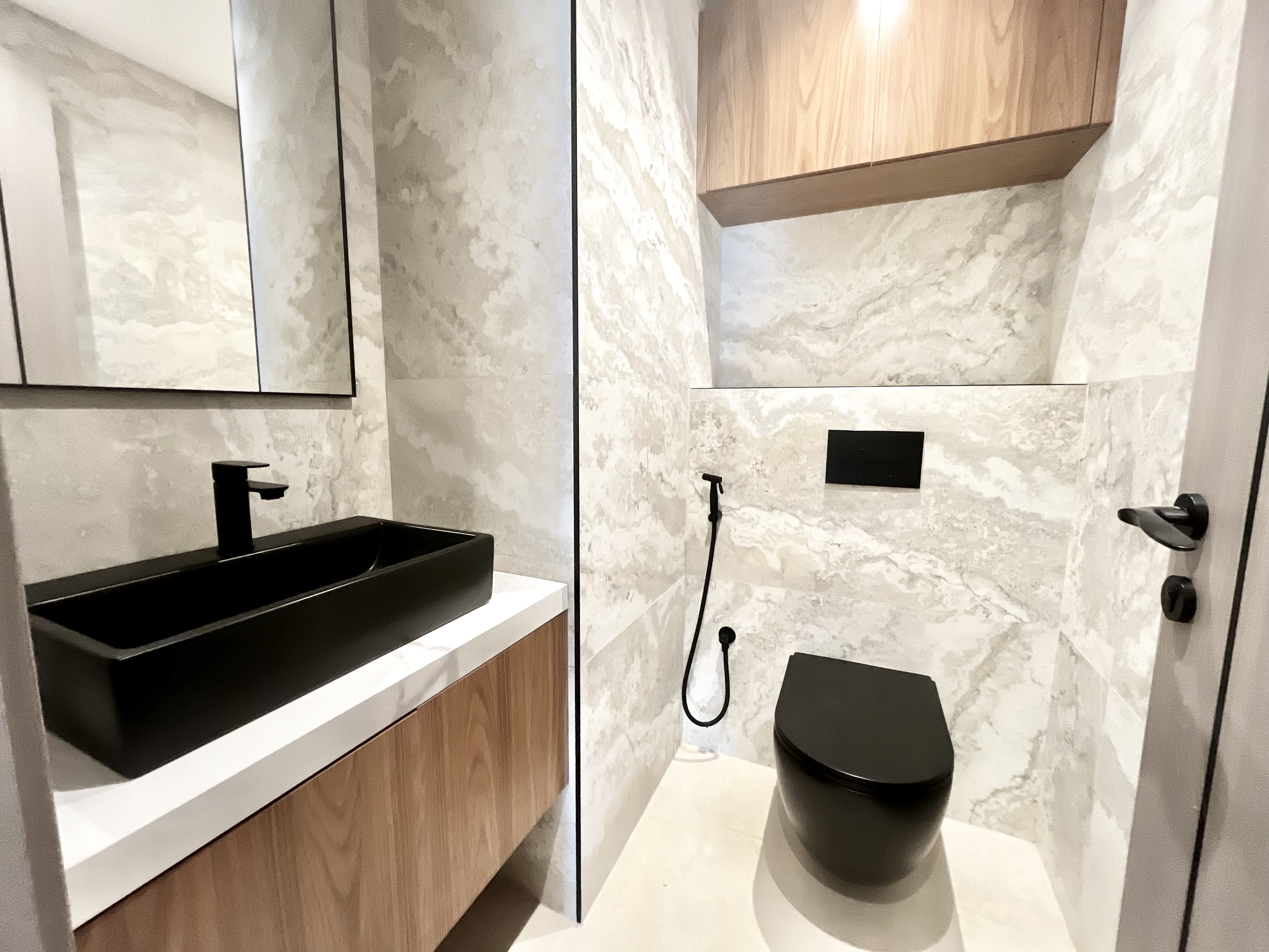 Modern bathroom with marble-patterned walls, a black vessel sink, a black toilet, and light wood cabinetry.
