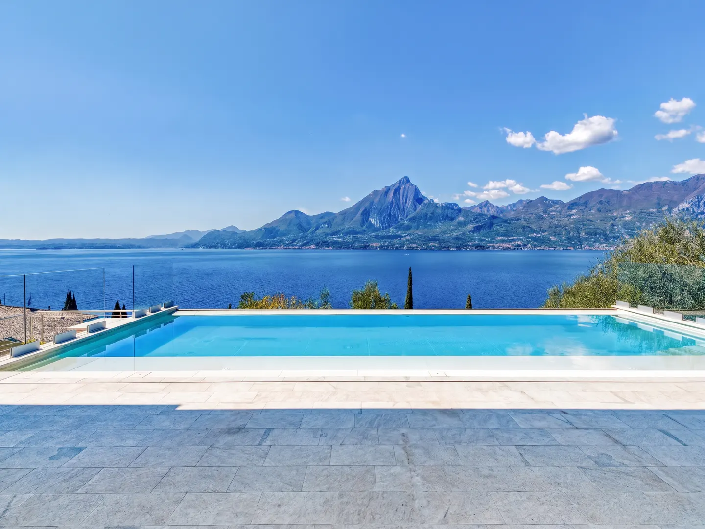 Infinity pool with blue water overlooking a lake and mountains under a blue sky.