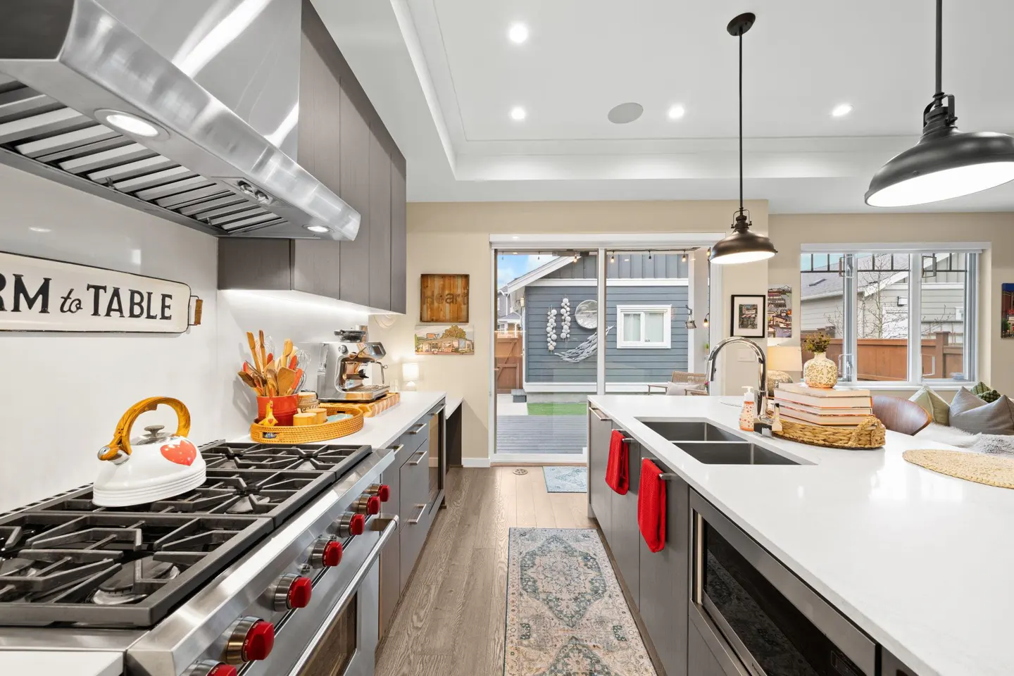Bright kitchen with gray cabinets, white countertops, and stainless steel appliances. A sliding glass door leads to a backyard.