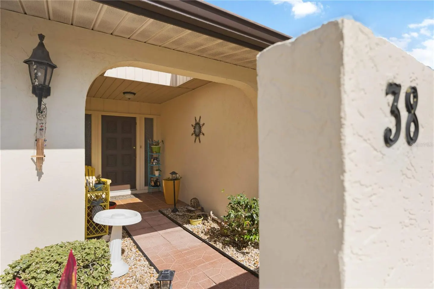 Exterior view of a home's entrance with a beige stucco wall, black house number 38, and a walkway leading to the front door.
