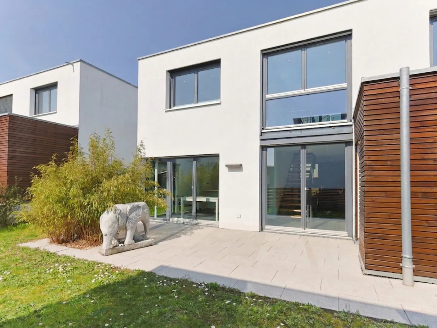 Modern white house with large windows, a stone patio, and a small elephant statue in the yard.