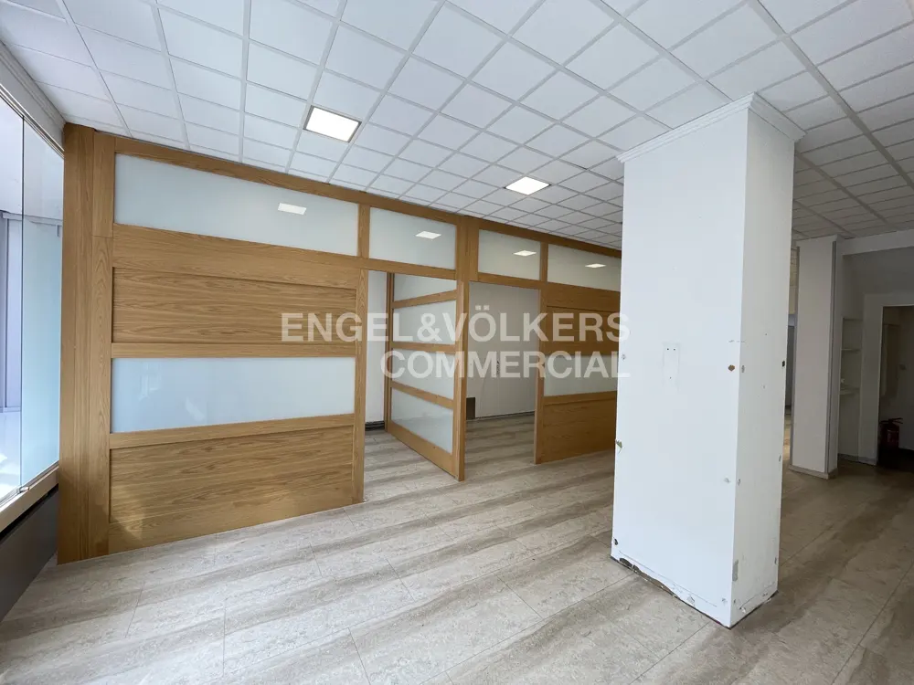 Empty office space with wood and frosted glass dividers, light tile floor, and white ceiling with recessed lighting. Engel & Völkers Commercial logo.
