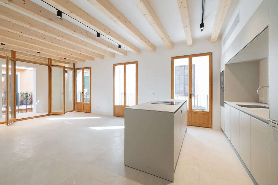 Bright, modern kitchen with white walls, light wood beams, and a gray island. Wood-framed glass doors lead to balconies.