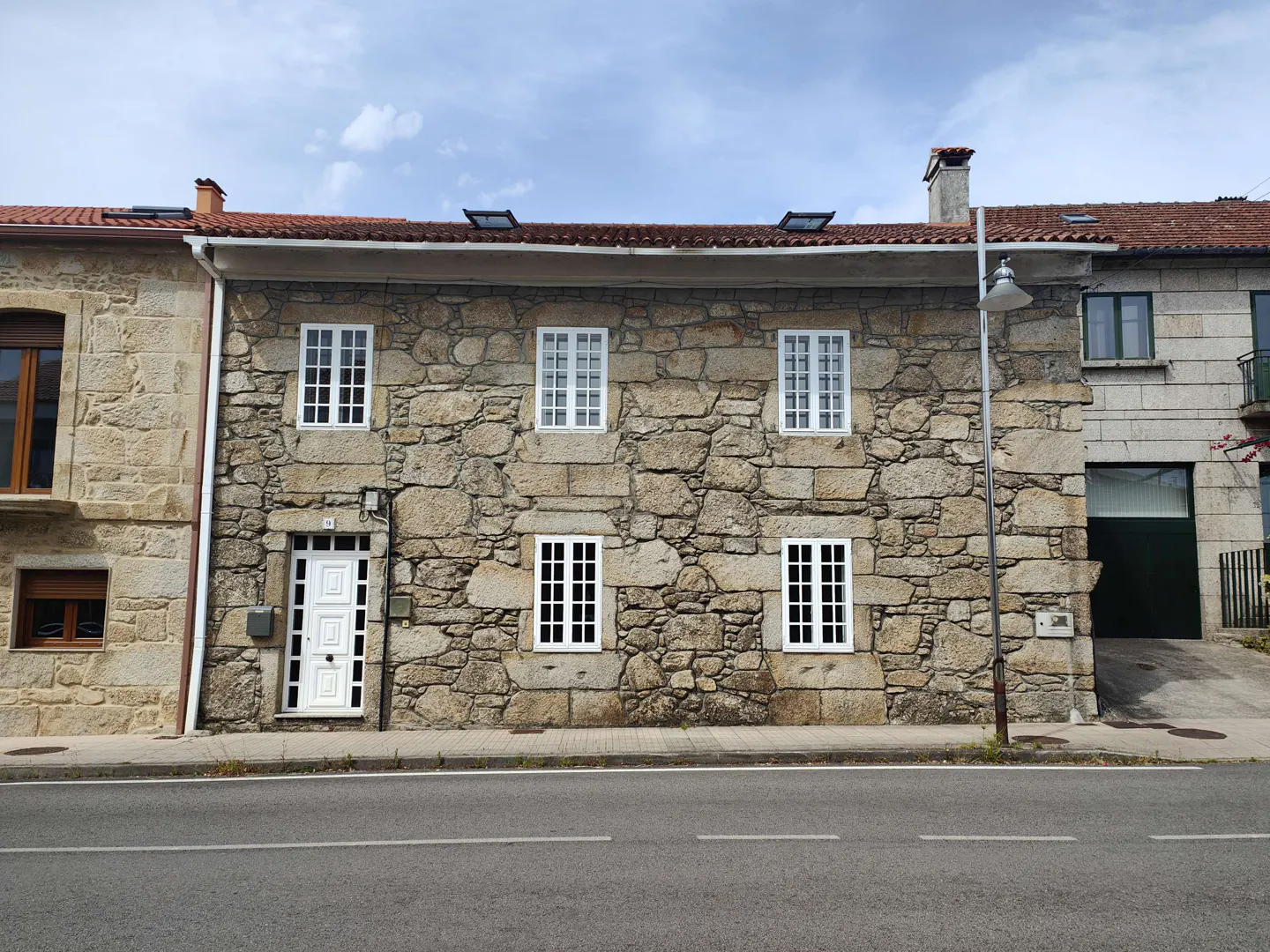 Stone house with white windows and door, red tile roof, and street in front.